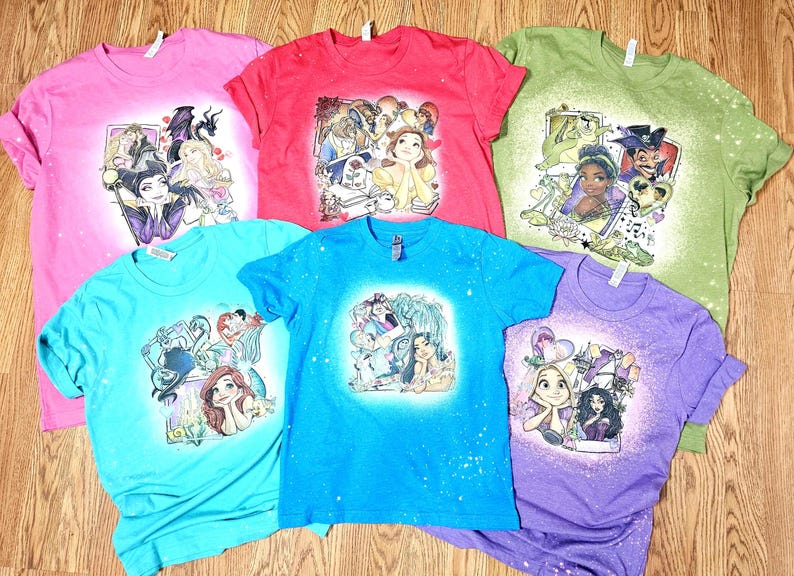 May include: Six different t-shirts with bleach-splattered designs featuring Disney princesses and villains. The shirts are in various colours, including pink, red, green, blue, and purple.