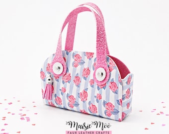 Op de afbeelding: Een kleine handtas met een lichtblauw en wit verticaal gestreept patroon met roze rozen. Het heeft twee roze glitterhandvatten bevestigd met zilveren drukknopen en een kleine roze kwastbedel. De tekst Maisie Moo Faux Leather Crafts is zichtbaar.