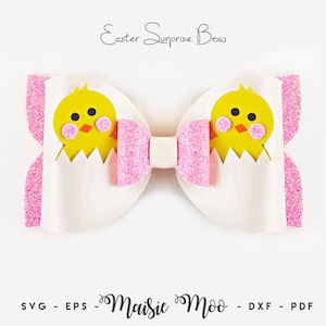 Könnte beinhalten: Eine Haarschleife mit dem Text Easter Surprise Bow oben und Maisie Moo SVG - EPS - DXF - PDF unten. Die Schleife ist weiß mit rosa Glitzerakzenten und zwei gelben Küken, die aus weißen Eierschalen schlüpfen und rosa Wangen haben.