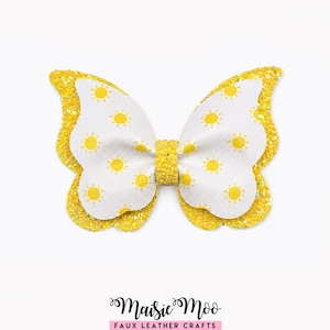 May include: A butterfly-shaped hair bow featuring a white top layer with a yellow sun pattern and a yellow glittery bottom layer. The center is wrapped in yellow glitter material. The text Maisie Moo Faux Leather Crafts appears below.