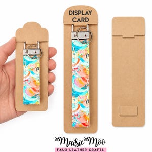 May include: Two keychains with a colorful abstract pattern of teal, orange, and pink shapes on a white background, featuring silver metal hardware and a split ring, attached to brown cardboard display cards with the text DISPLAY CARD printed.