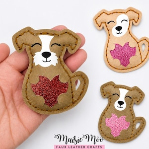 May include: Three dog-shaped faux leather appliqués with stitched edges. Each features a white face patch, closed eyes, and a glittery heart on the chest in red or pink. The text Maisie Moo Faux Leather Crafts is printed at the bottom of the image.