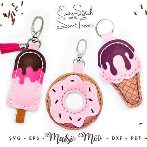 Può includere: Tre portachiavi con un cono gelato rosa e marrone, un donut rosa e marrone e un ghiacciolo rosa e marrone. I portachiavi sono etichettati "Easy Stitch Sweet Treats" e "Maisie Moo".