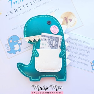 May include: A teal faux leather dinosaur-shaped pouch with a white pocket containing a one-dollar bill. The dinosaur features a pink cheek, white teeth, and white dorsal spikes. It is displayed with a tooth certificate and a poem card.