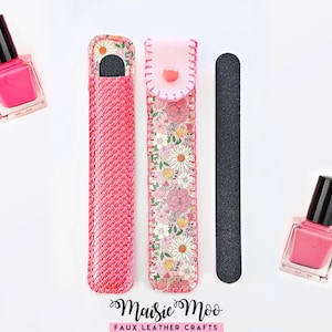 Könnte beinhalten: Zwei Fläschchen mit leuchtend pinkem Nagellack, eine schwarze Nagelfeile und eine Schutzhülle für die Feile. Die Hülle hat auf einer Seite eine geflochtene pinke Textur und auf der anderen ein Blumenmuster mit Gänseblümchen und Rosen, verschlossen mit einem pinken Druckknopf.