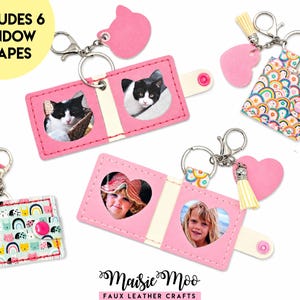 May include: Pink faux leather keychains with various shapes, including cat faces and hearts. Some keychains feature photos of cats and children. The keychains have metal clasps and decorative tassels. The text "INCLUDES 6 WINDOW SHAPES" is visible.