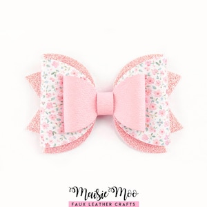 Puede incluir: Un lazo para el pelo en capas con una pieza central de piel sintética rosa claro, flanqueada por dos paneles blancos con un pequeño estampado floral rosa y una base de material con purpurina rosa texturizada. El texto Maisie Moo Faux Leather Crafts aparece debajo.