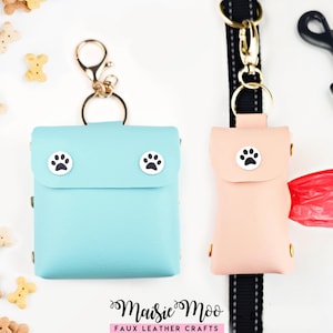 May include: A light blue square pouch and a light peach rectangular pouch, both featuring white circular paw print accents. The peach pouch is attached to a black lead and contains a red plastic bag. The text Maisie Moo Faux Leather Crafts is visible.