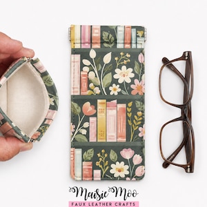 Peut inclure: Une petite pochette à monnaie ouverte et un étui à lunettes rectangulaire avec un fond vert foncé orné d'un motif de livres colorés et d'illustrations florales. Le texte Maisie Moo Faux Leather Crafts est imprimé en bas de l'image.