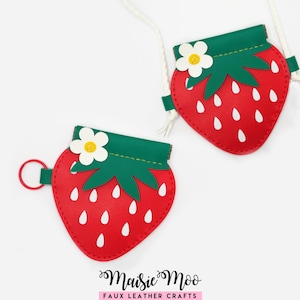 May include: Two red strawberry-shaped pouches with green tops and white seed details. Each pouch has a white flower accent and a white cord. One pouch has a red ring. The text "Maisie Moo Faux Leather Crafts" is at the bottom.