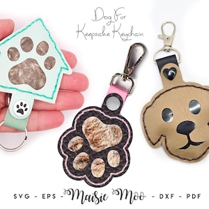May include: Three dog fur keepsake keychains. One is a light blue house shape with a paw print, another is a paw print shape with a pink strap, and the last is a tan dog face. The keychains have metal clasps.