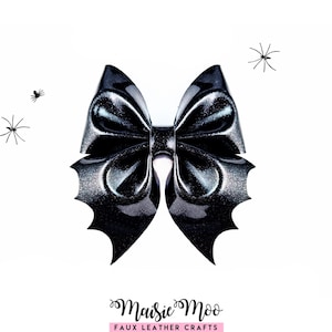 May include: A black glittery bow with bat-wing shaped edges, featuring a central knot. Three small black spider illustrations are positioned around the bow. The text Maisie Moo FAUX LEATHER CRAFTS is printed in black and pink at the bottom.