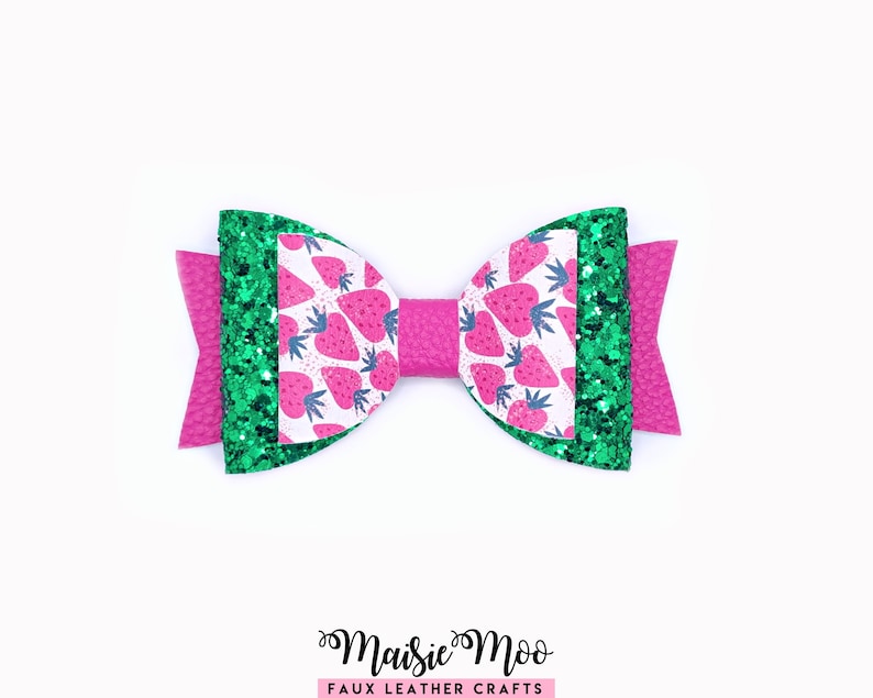 May include: A handmade bow featuring a strawberry pattern on white, green glitter accents, and a bright pink base. The bow is made of faux leather and has a textured finish. The text "Maisie Moo Faux Leather Crafts" is at the bottom.