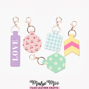 May include: Five faux leather keychains with rose gold hardware. One is a purple rectangle with the word LOVE, one is a pink circle with a cherry print, one is a light blue gingham square, one is a yellow chevron arrow, and one is a mint hexagon with daisies.