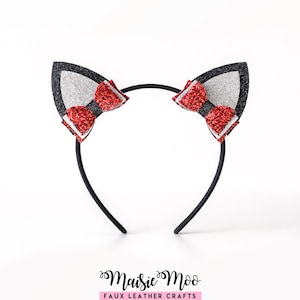 May include: A black headband featuring two cat ears made of black glitter fabric with silver glitter inner sections. Each ear is decorated with a small, layered red glitter bow. The text Maisie Moo FAUX LEATHER CRAFTS is printed below.
