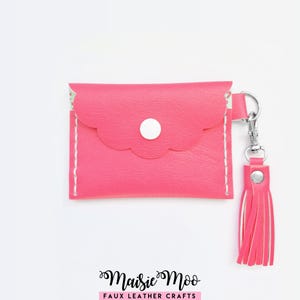 May include: A bright pink faux leather coin purse featuring a scalloped flap, a white snap button closure, and white stitching along the sides. A matching pink faux leather tassel is attached to the side with a silver metal lobster clasp.