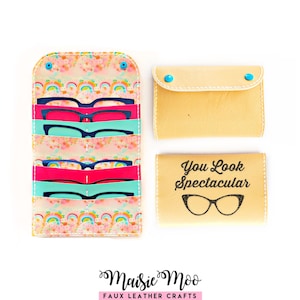May include: A multi-slot organizer case featuring a colorful rainbow and floral pattern, holding several pairs of dark-rimmed glasses. Beside it are two tan faux leather cases, one with the text You Look Spectacular and a glasses graphic.