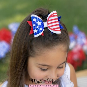 Op de afbeelding: Een patriottische haarstrik met rode, witte en blauwe kleuren. De strik heeft een wit midden, rood-witte strepen aan &eacute;&eacute;n kant en een blauw gedeelte met witte sterren aan de andere kant. Bevestigd met een zwarte haarband.