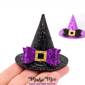 May include: Black glitter witch hat with a purple bow and gold buckle. A second purple witch hat is in the background. The hats are likely for Halloween or costume use.
