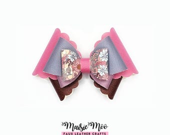 May include: A multi-layered hair bow featuring scalloped edges in pink, metallic lavender, and dark brown faux leather. The center is accented with a floral patterned fabric piece. Below the bow, the text reads Maisie Moo FAUX LEATHER CRAFTS.