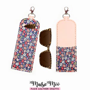 May include: A floral print sunglasses case with a clip, next to a pair of leopard print sunglasses. The case is navy blue with a colorful floral pattern and a pink top. The case is made of faux leather.