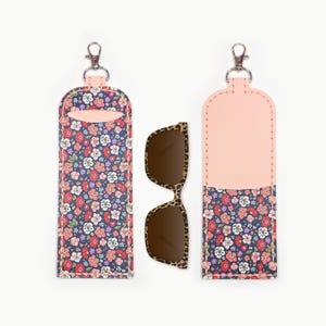 May include: A floral print sunglasses case with a matching pair of leopard print sunglasses. The case is navy blue with a colorful floral pattern and a pink top. The sunglasses have a brown frame.