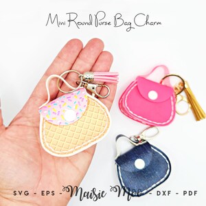 Peut inclure: Charm de sac en forme de mini sac &agrave; main, disponibles en rose, bleu jean et avec un motif gaufre. Le sac &agrave; main gaufre a un rabat avec des paillettes color&eacute;es. Chaque breloque comprend un porte-cl&eacute;s et un pompon. Le texte "Mini Round Purse Bag Charm" et "Maisie Moo" sont visibles.
