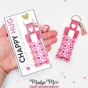 May include: A pink lip balm holder with a heart pattern and a tassel. The holder is attached to a keyring and is displayed with a card that says "CHAPPY HUG KEEP YOUR LIP BALM SNUG".