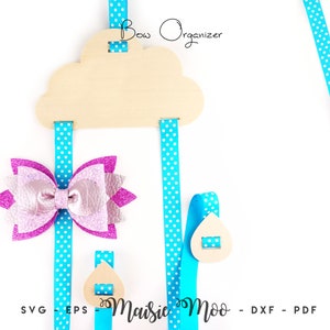 May include: A wooden cloud-shaped bow organizer with blue and white polka dot ribbon holders. The organizer has a "Bow Organizer" title and is hanging from the top. A pink and purple bow is displayed on the organizer.