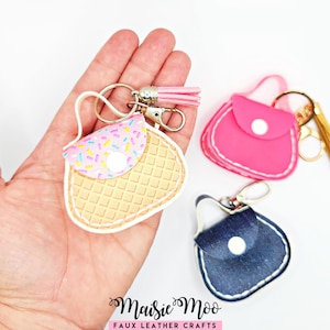 May include: Three miniature handbag keychains with metal clasps and tassels. One features a waffle-textured tan base with a pink sprinkle-patterned flap. Another is solid hot pink, and the third is dark blue denim-textured, each with a white snap.