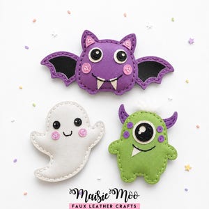 May include: Three faux leather craft appliques featuring a purple bat with black wings, a white ghost, and a green one-eyed monster with purple horns. The text Maisie Moo Faux Leather Crafts is printed at the bottom of the white background.