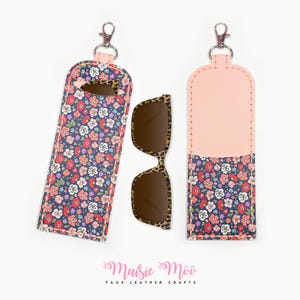 May include: A floral print sunglasses case with a matching pair of sunglasses. The case is navy blue with a colorful floral pattern and a pink top. The sunglasses have a leopard print frame.