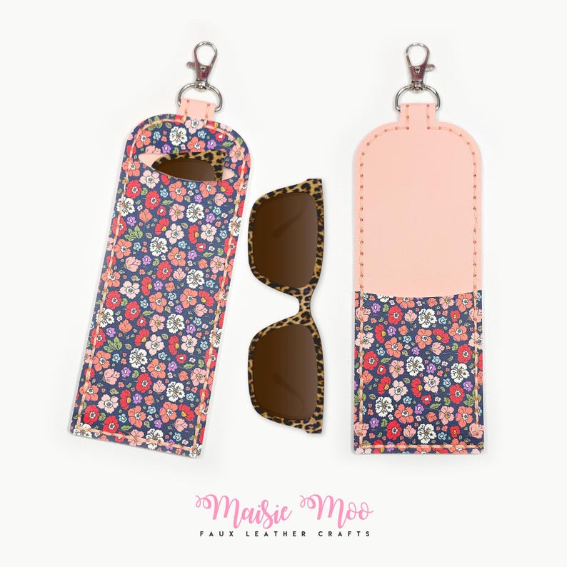 May include: A floral print sunglasses case with a matching pair of sunglasses. The case is navy blue with a colorful floral pattern and a pink top. The sunglasses have a leopard print frame.
