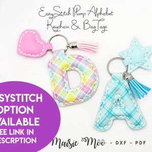 May include: Two colorful plaid fabric letters, D and A, with a heart and star charm, attached to keychains. The letters are in a pastel plaid pattern, with pink, yellow, and blue colors. The heart charm is pink, and the star charm is blue. The text "Easy Stitch Pump Alphabet Keychain & Bag Tags" is at the top of the image. The text "EASYSTITCH OPTION AVAILABLE SEE LINK IN DESCRPTION Maisie Moo - DXF - PDF" is at the bottom of the image.