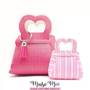 Op de afbeelding: Twee roze cadeauverpakkingen in de vorm van een handtas van imitatieleer. De grotere tas heeft een hartvormige handgreep en een roze kwastjes sleutelhanger. De kleinere tas heeft een roze en wit gestreept patroon. De tekst "Maisie Moo Faux Leather Crafts" staat onderaan.