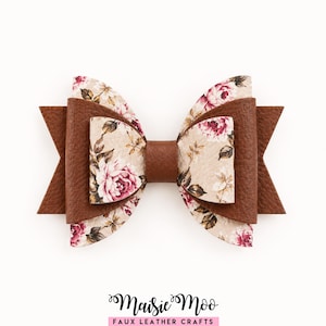 May include: A layered bow accessory featuring a combination of solid brown faux leather and a beige floral print fabric with pink roses and green leaves. The bow is constructed with a central brown knot and pointed side edges.