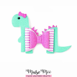 Op de afbeelding: Een turquoise haarclip in de vorm van een dinosaurus met een roze strik en accenten. De strik heeft witte strepen. De dinosaurus heeft een kleine roze strik op zijn hoofd. De clip is gemaakt van imitatieleer.