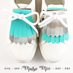 May include: A pair of white sneakers featuring removable shoe fringe attachments. The left fringe is turquoise over silver, while the right fringe is silver over turquoise. The text at the bottom reads SVG - EPS - Maisie Moo - DXF - PDF.