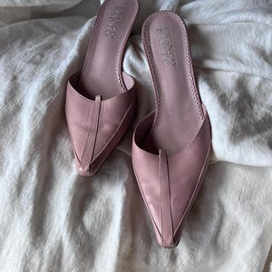 Peut inclure: Une paire de mules rose poudré Franco Sarto avec un bout pointu, une couture verticale au centre de l'empeigne et un bord festonné le long de la semelle intérieure. Le nom de la marque Franco Sarto est imprimé sur le talon de chaque chaussure.