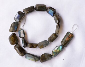 May include: A strand of dark gray labradorite gemstone beads with iridescent blue and green flashes. The beads are faceted and have a rectangular shape. The strand is approximately 18 inches long.
