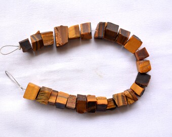 May include: A strand of tiger's eye beads featuring irregular, cube-like shapes with natural brown and golden-yellow banded patterns. The beads are strung on a thin metal wire, showcasing a variety of earthy tones and polished, reflective surfaces.