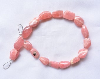 May include: A strand of pink and white gemstone beads, strung on a silver wire. The beads are irregularly shaped and have a natural, polished finish.