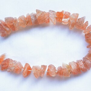 May include: A strand of sunstone beads, strung on wire, with a natural, irregular shape. The beads are a light orange color with a slight shimmer.