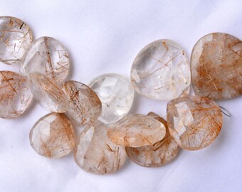 May include: A collection of twelve clear quartz beads with brown inclusions. The beads are faceted and have a teardrop shape.