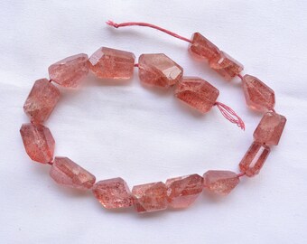 May include: A strand of faceted, translucent pink and red gemstone beads. The beads are strung on a thin red thread.