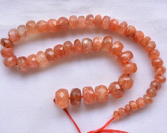 May include: A strand of orange sunstone beads with a faceted finish. The beads are strung on a red thread and are approximately 10mm in diameter.