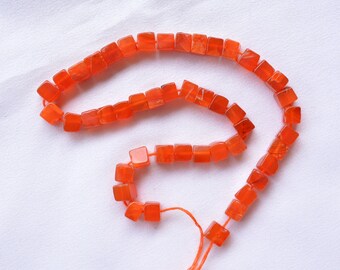 May include: A strand of orange carnelian gemstone beads, each bead is a cube shape. The beads are strung on a thin thread and are ready to be used for jewelry making.