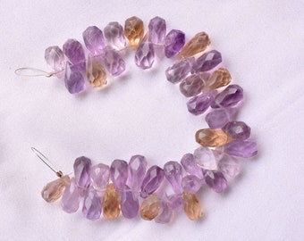 May include: A strand of faceted gemstone beads in shades of purple and amber. The beads are teardrop shaped and strung on a wire.