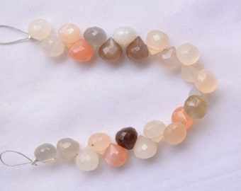 May include: A strand of faceted gemstone beads in shades of white, gray, pink, and brown. The beads are teardrop shaped and strung on a silver wire.