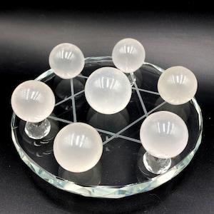 May include: Seven white selenite spheres arranged in a circle on a clear glass base with a geometric design. The spheres are smooth and polished.